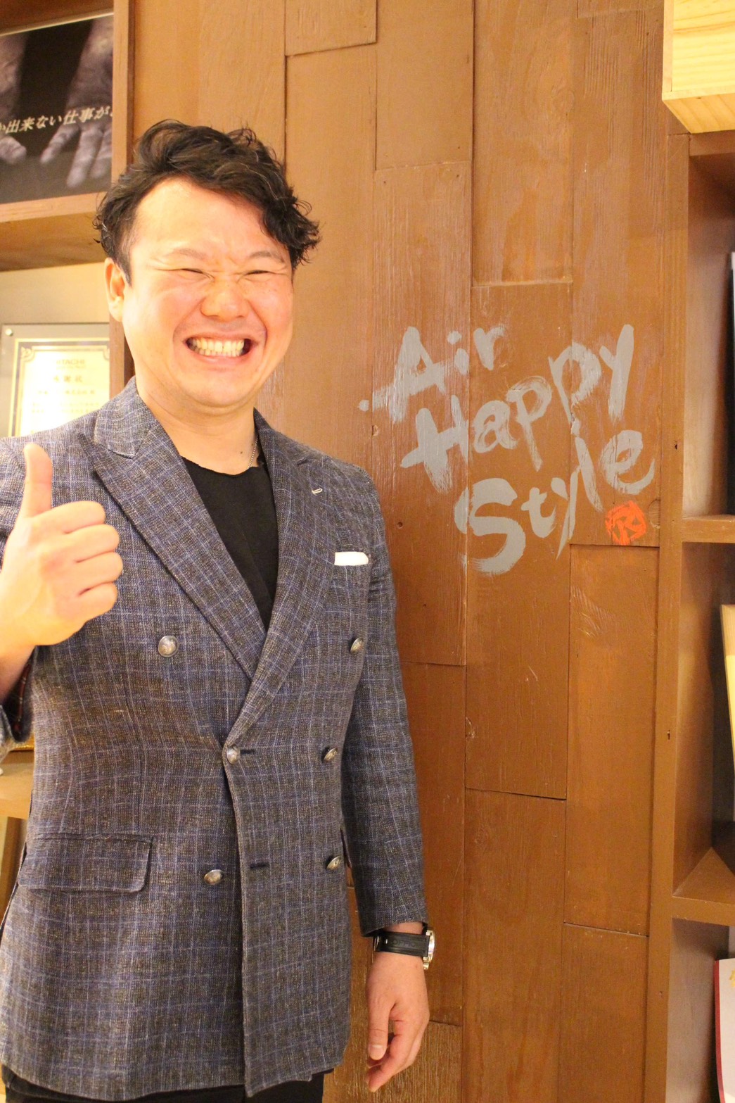 AIR HAPPY STYLEの壁の前で笑顔を見せる代表取締役 伊藤丈史